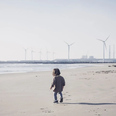 Child walking in the beach close to wind farm