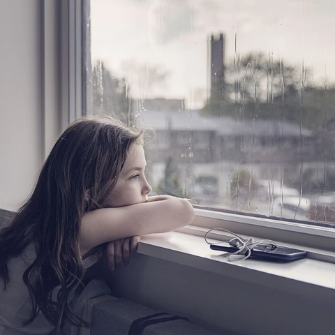 Young girl looking out of window on a rainy day