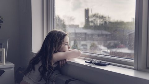 Young girl looking out of window on a rainy day