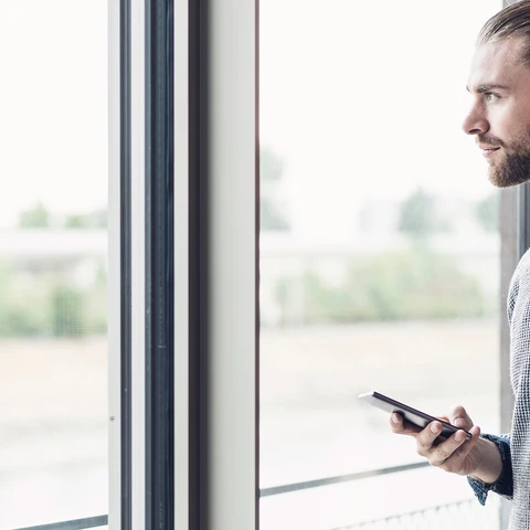 Young businessman with cell phone looking out of window