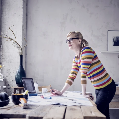 Portrait of smiling woman standing at desk in a loft looking through window