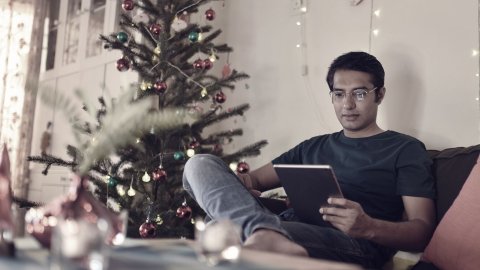 man sitting next to a christmas tree reading on his ipad