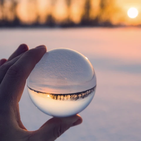 Hand holding a crystal ball with snowy sunset in the background