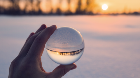 Hand holding a crystal ball with snowy sunset in the background