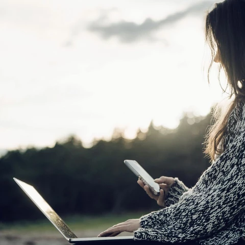 Woman with laptop text messaging while sitting at beach
