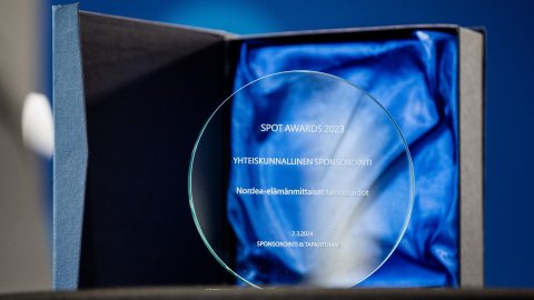 Kuva SPOT Award-pystistä, joka on pyöreä läpinäkyvä kiekko johon on kirjoitettu tiedot palkinnosta.