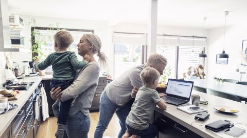 Isä, äiti ja kaksi pientä poikaa viettävät aikaa keittiössä. Isä ja toinen pojista katsoo yhdessä tietokonetta ja toinen lapsista on äidin sylissä.