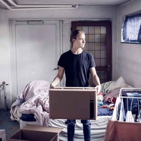 Man carrying cardboard box while standing in bedroom