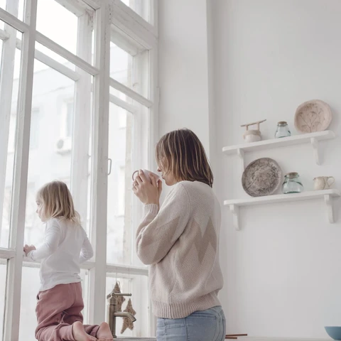 Nainen ja tyttö katsovat ulos isosta ikkunasta vaaleansävyisessä huoneessa.