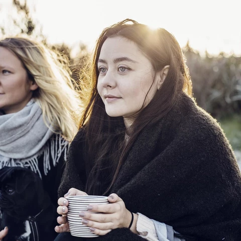 thoughtful-female-friends-sitting-with-dog-on-beach