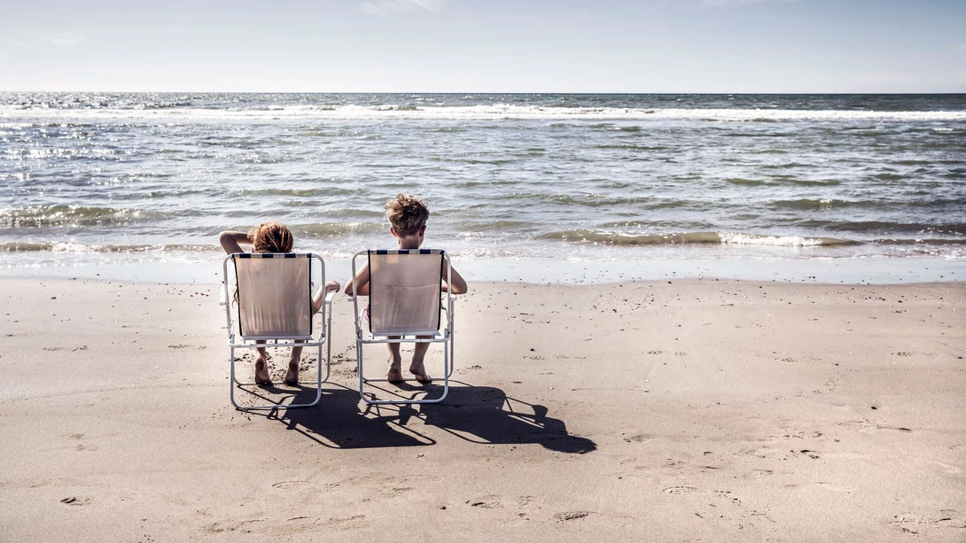 Boy and girl sitting on chairs on the beach