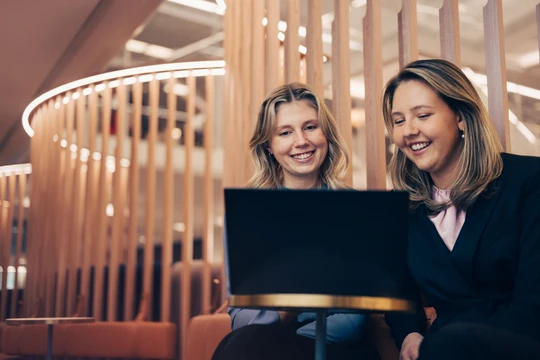 Two students smiling and looking at laptop